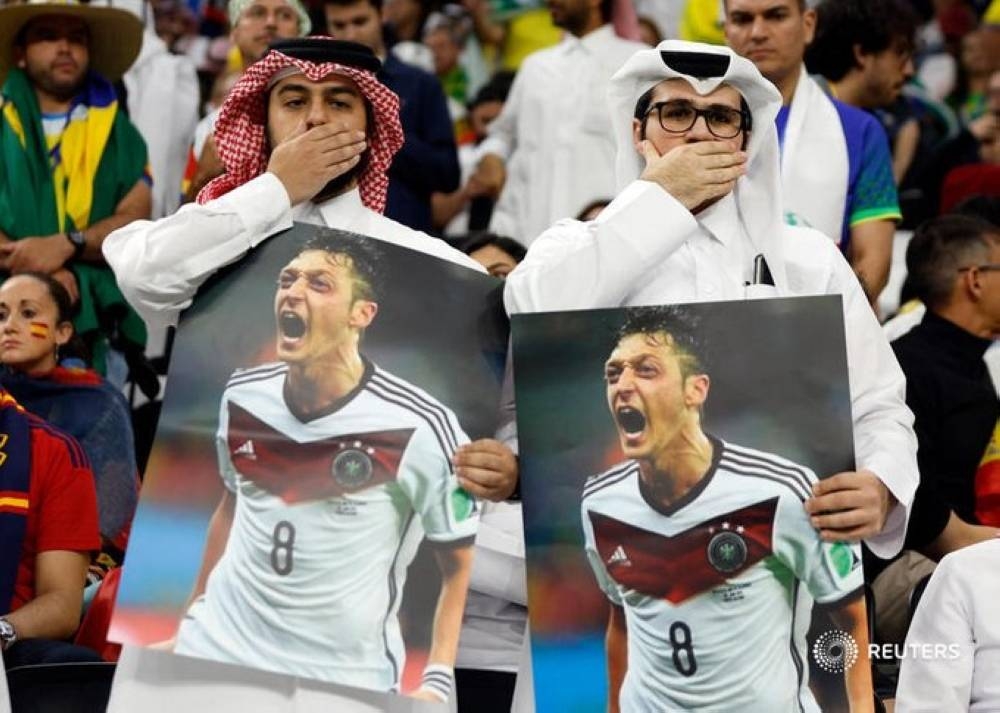 Fans cover their mouths while holding pictures of former Germany player Mesut Ozil at Al Bayt Stadium