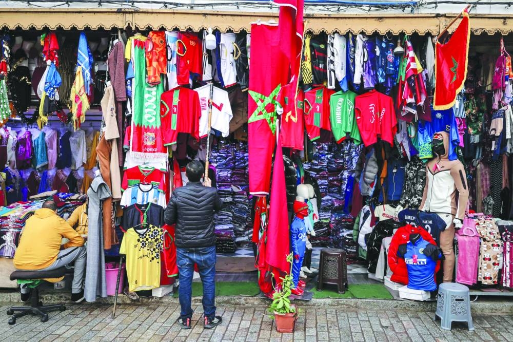 A shop keeper hangs a football jersey among flags at a sports apparel shop in the capital Rabat, Morocco yesterday, a day ahead of the Qatar 2022 FIFA World Cup semi-final match agaisnt France. (AFP)