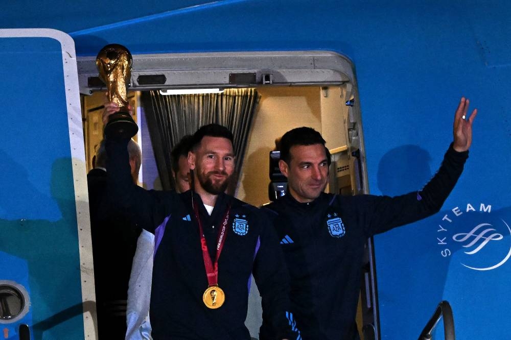 Argentina's captain and forward Lionel Messi holds the FIFA World Cup Trophy alongside Argentina's coach Lionel Scaloni as they step off a plane upon arrival at Ezeiza International Airport after winning the Qatar 2022 World Cup tournament. (AFP)