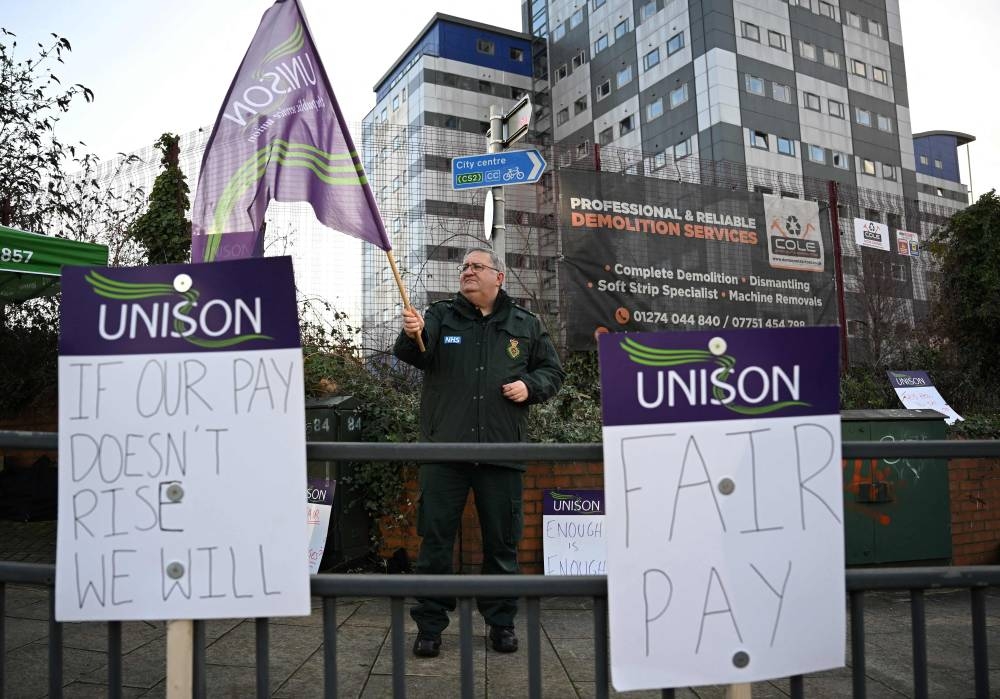 An ambulance worker waves a flag of the UK's trade union UNISON as he stands on a picket line in Leeds (AFP)