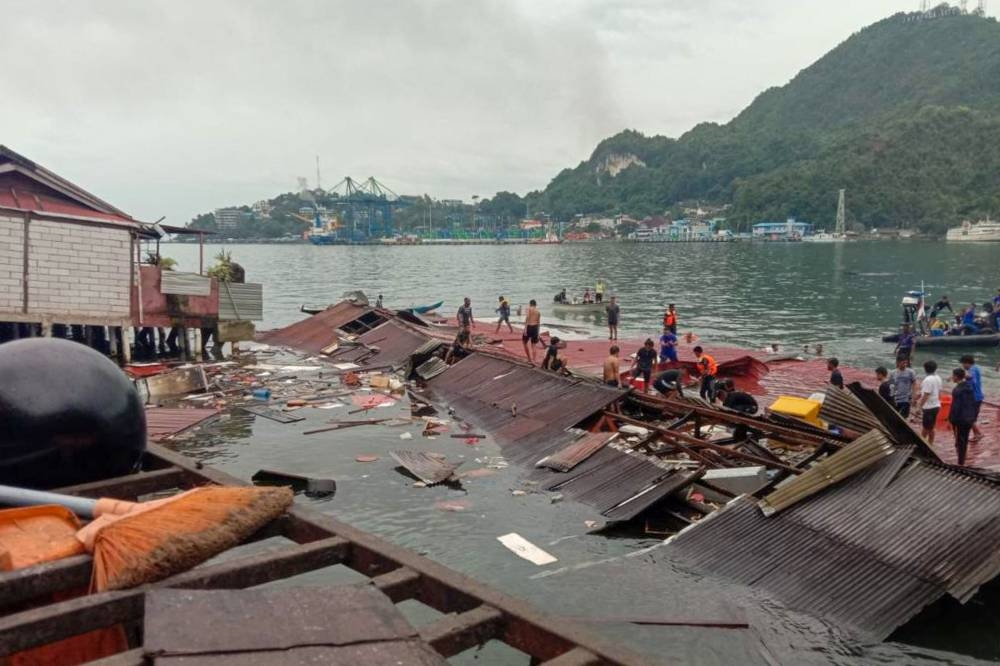 People stand on the roofing of collapsed shops in the port after a 5.1-magnitude earthquake in Jayapura, Indonesia's eastern province of Papua on February 9, 2023. (AFP)