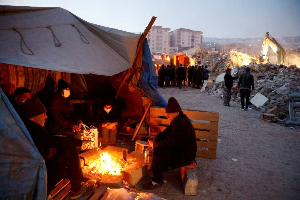People sit around a fire near the site of a collapsed building, as the search for survivors continues, in the aftermath of an earthquake, in Kahramanmaras, Turkey, Thursday. REUTERS