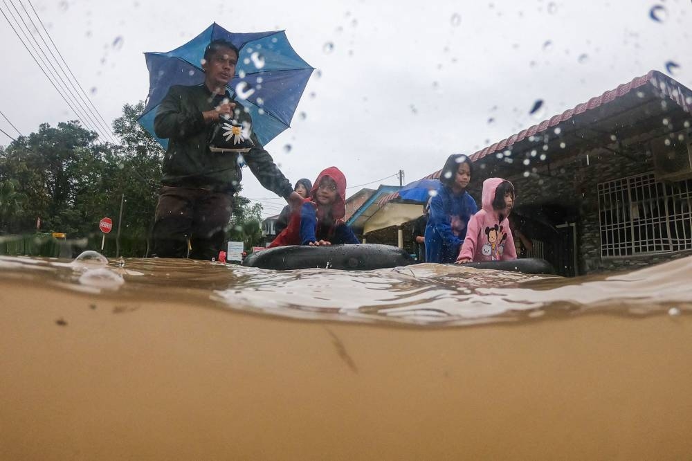 A family wade through floodwaters after evacuating their home in a flooded area in Yong Peng, Malaysia's Johor state on March 4, 2023. (Photo by Mohd RASFAN / AFP)