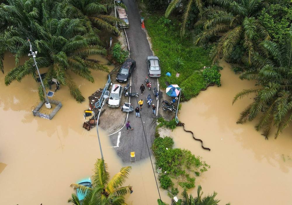 An aerial view shows people standing on a flooded road in Yong Peng, Malaysia's Johor state, on March 4, 2023. - At least four people have died and nearly 41,000 evacuated in Malaysia after floodwaters caused by "unusual" torrential rains lasting days swept through several states, officials said March 4. (Photo by Mohd RASFAN / AFP)