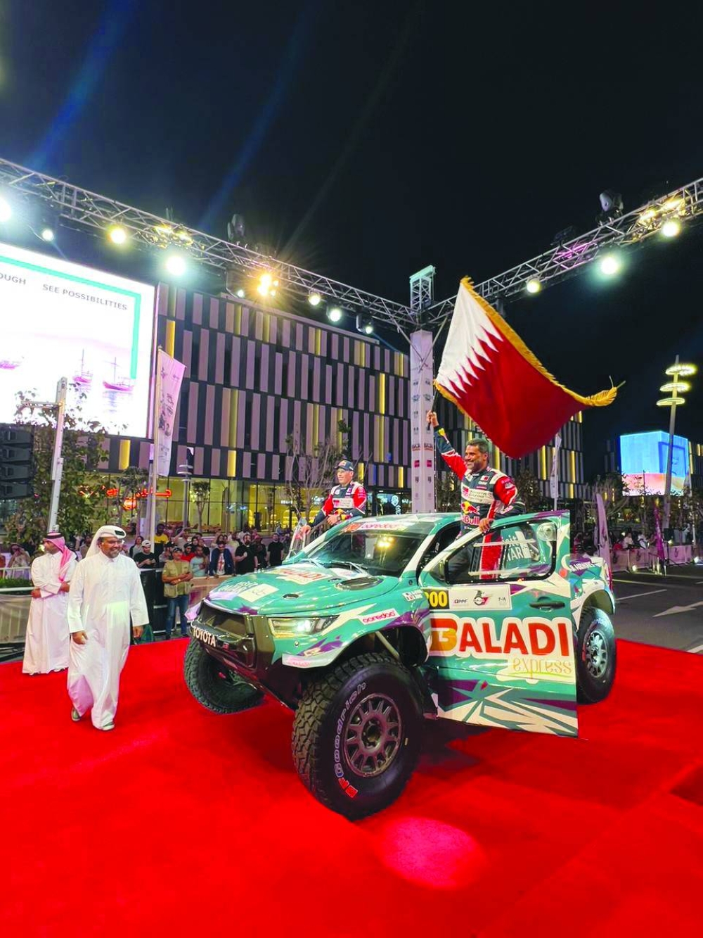    Nasser Saleh al-Attiyah waves the Qatar flag as Qatar Motor and Motorcycle Federation (QMMF) President Abdulrahman bin Abdullatif al-Mannai looks on during the ceremonial start of the Qatar International Baja at the Lusail Boulevard yesterday.


