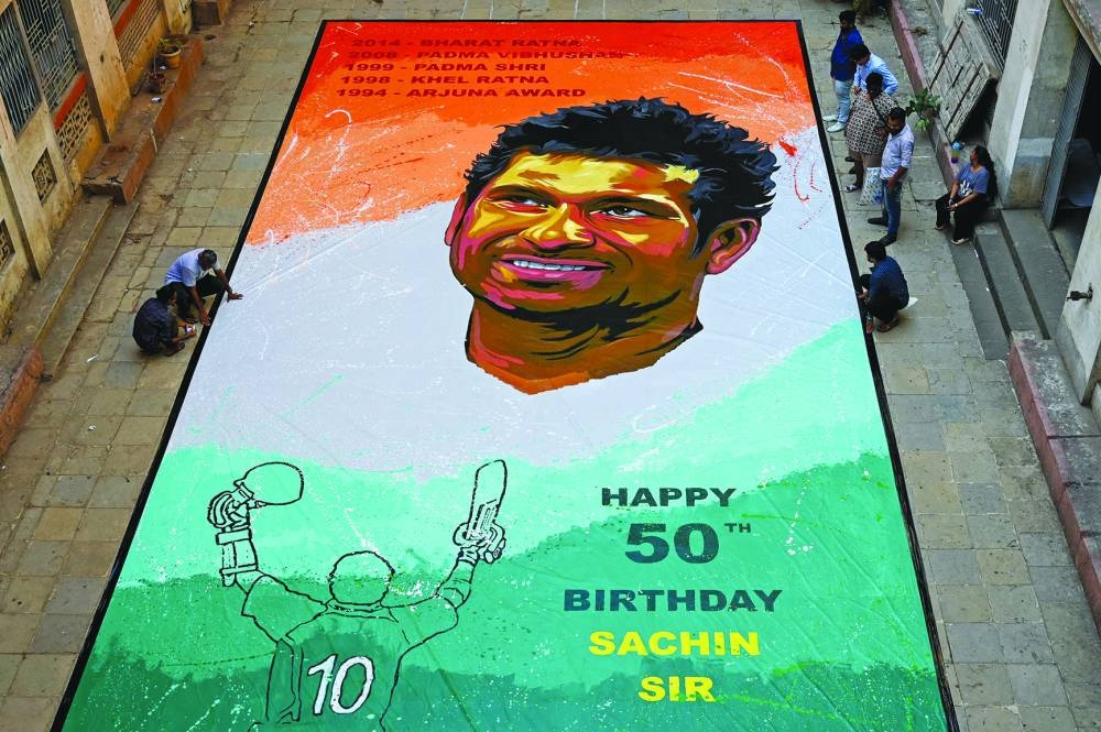 People stand near a painting of Indian former international cricketer Sachin Tendulkar made on the occasion of his 50th birthday, in Mumbai on Monday. (AFP)