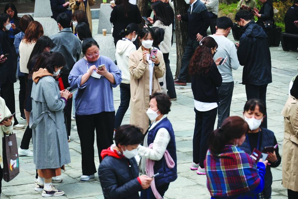 Office workers look at their mobile phones to check the local online banking app Toss as they gather at Seoul Museum of Art during a lunch break in Seoul, South Korea