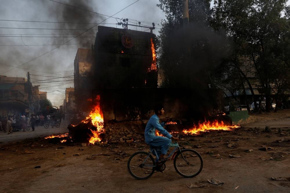 A boy rides past a paramilitary check post, that was set afire by the supporters of Pakistan's former Prime Minister Imran Khan, during a protest against his arrest, in Karachi, Pakistan. REUTERS/Akhtar Soomro