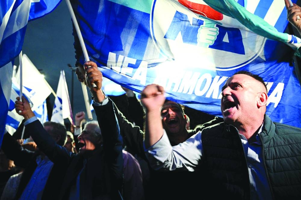 People wave the New Democracy's flag after the announcement of the first exit polls in front of the right wing party New Democracy's headquarters, in central Athens on Sunday. (AFP)