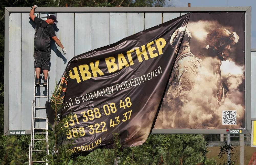 A worker removes an advertising banner promoting service in Wagner private mercenary group on the outskirts of Saint Petersburg, Russia. A slogan on the banner reads: "Accede to the team of victors!" REUTERS/Anton Vaganov