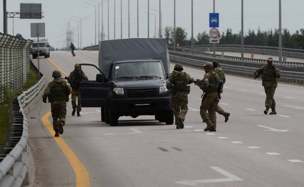 Fighters of Wagner private mercenary group walk around a vehicle during a stop on M-4 highway, which links the capital Moscow with Russia's southern cities, with smoke from a burning fuel tank at an oil depot seen in the background, near Voronezh, Russia. REUTERS/Stringer