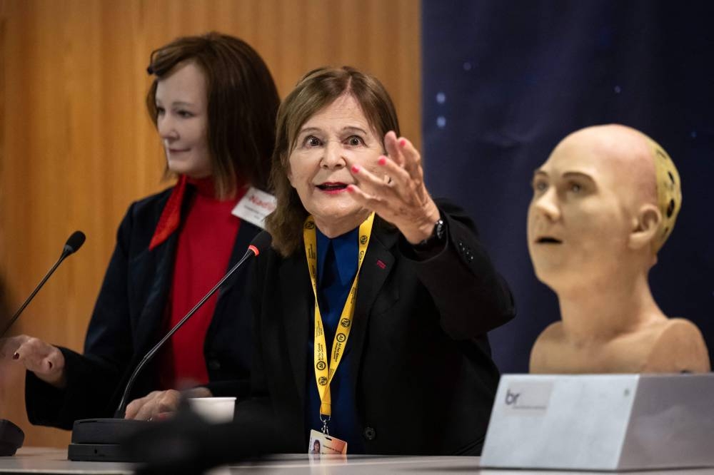 Professor Nadia Magnenat Thalmann (C) gestures next to AI-powered humanoid social robot "Nadine" (L) during what was presented as the World's first press conference with a panel of AI-enabled humanoid social robots as part of International Telecommunication Union (ITU) AI for Good Global Summit in Geneva. Fabrice COFFRINI / AFP