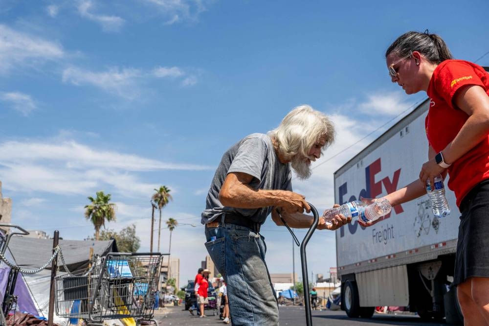 A volunteer with the Wells Fargo Technology Services passes out water to a homeless resident on July 14 in Phoenix, Arizona. Getty Images via AFP