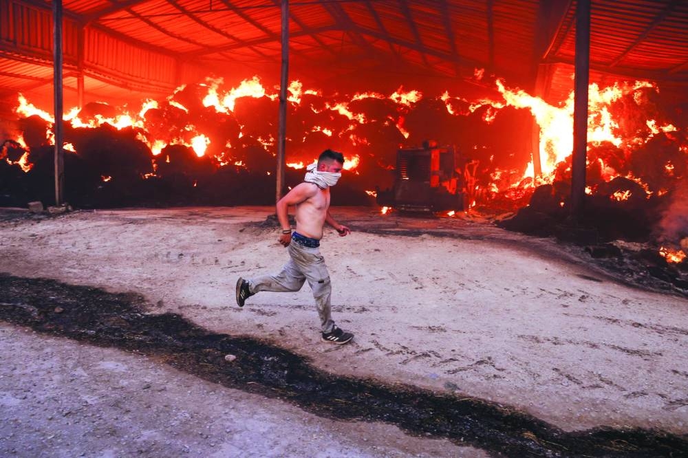 
A young man runs next to a burning farm, as a wildfire burns in Sesklo, in central Greece, yesterday. Right:  Large plumes of smoke billowing from wildfires raging across the island of Rhodes. (Reuters, AFP) 