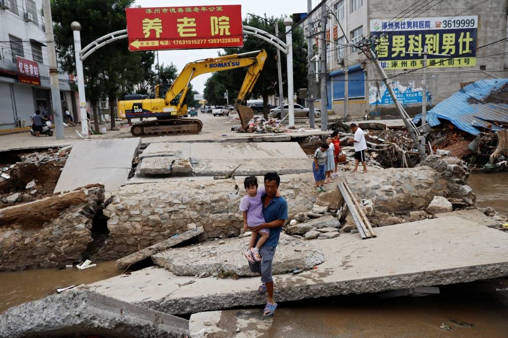 A man holding a child walks across a damaged bridge after the rains and floods brought by remnants of Typhoon Doksuri, in Zhuozhou, Hebei province, China. REUTERS/Tingshu Wang
