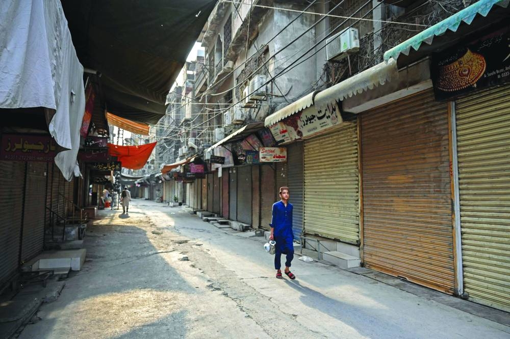 
A boy walks past closed shops along a street in Peshawar yesterday during a nationwide strike by traders against the surge in electricity and fuel prices. Right: Rickshaw drivers wait for customers along a street in Karachi during the strike. (AFP) 