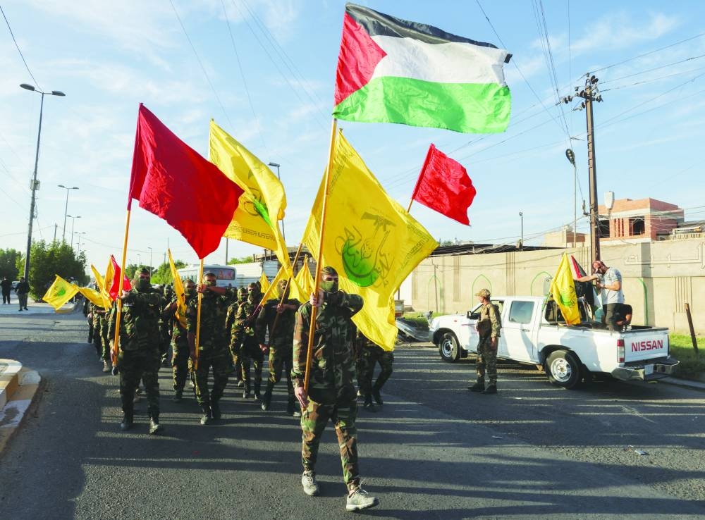 
People inspect the ruins of a building destroyed in Israeli strikes in Gaza City, yesterday. Right: Members of Harakat Hezbollah Al Nujaba, hold a Palestinian flag and other flags during a protest in solidarity with Palestinians in Gaza, in Baghdad, Iraq, yesterday. 