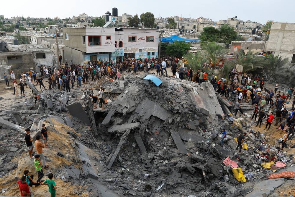 Palestinians gather around the rubble of a building destroyed in Israeli strikes, in the southern Gaza Strip Monday. REUTERS