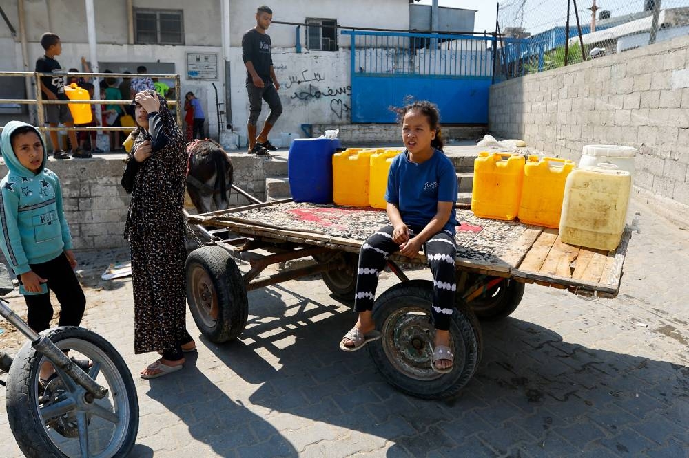 A girl sits next to a container as Palestinians gather to fill water from public taps amid the conflict with Israel in Khan Younis, in the southern Gaza Strip Wednesday. REUTERS