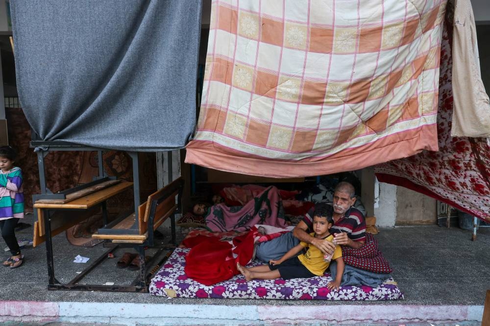 An internally displaced Palestinian man sits with a child on a mattress on the ground as they rest as they take refuge in a United Nations school, in the Rafah refugee camp, in the southern of Gaza Strip Saturday. AFP