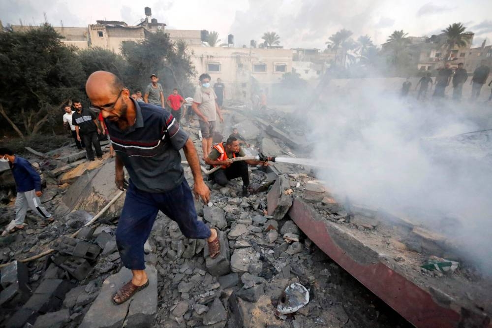 A Palestinian civil defence operator sprays water to douse the area as he squats atop of the rubble of a building destroyed following an Israeli attack on the town of Deir Al-Balah, in the central Gaza Strip, on Sunday. AFP