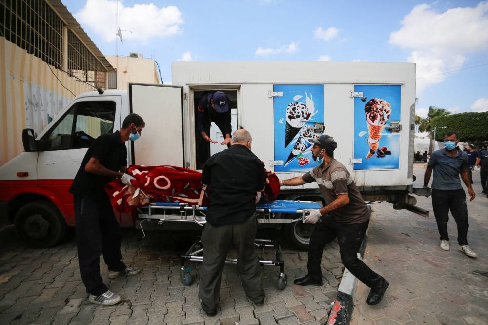 People carry the body of a Palestinian, who was killed in Israeli strikes, from an ice cream truck where it was kept, as the hospital morgues are packed, amid the ongoing Israeli-Palestinian conflict, in the central Gaza Strip Sunday. REUTERS