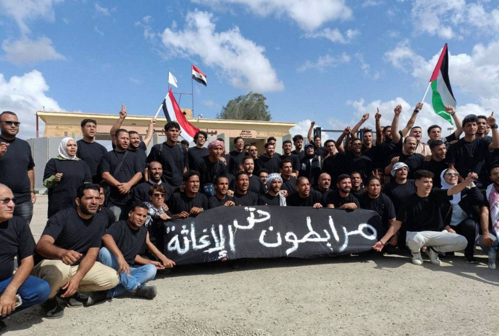 Egyptian volunteers shout slogans, with a banner that reads "Standing solid until relief", after a blast at a hospital in Gaza on October 17, in front of the Rafah crossing, as trucks carrying humanitarian aid for Palestinians await a decision for it to open to enter Gaza, amid the ongoing conflict between Israel and the Palestinian Islamist group Hamas, in Rafah, Egypt Wednesday. REUTERS