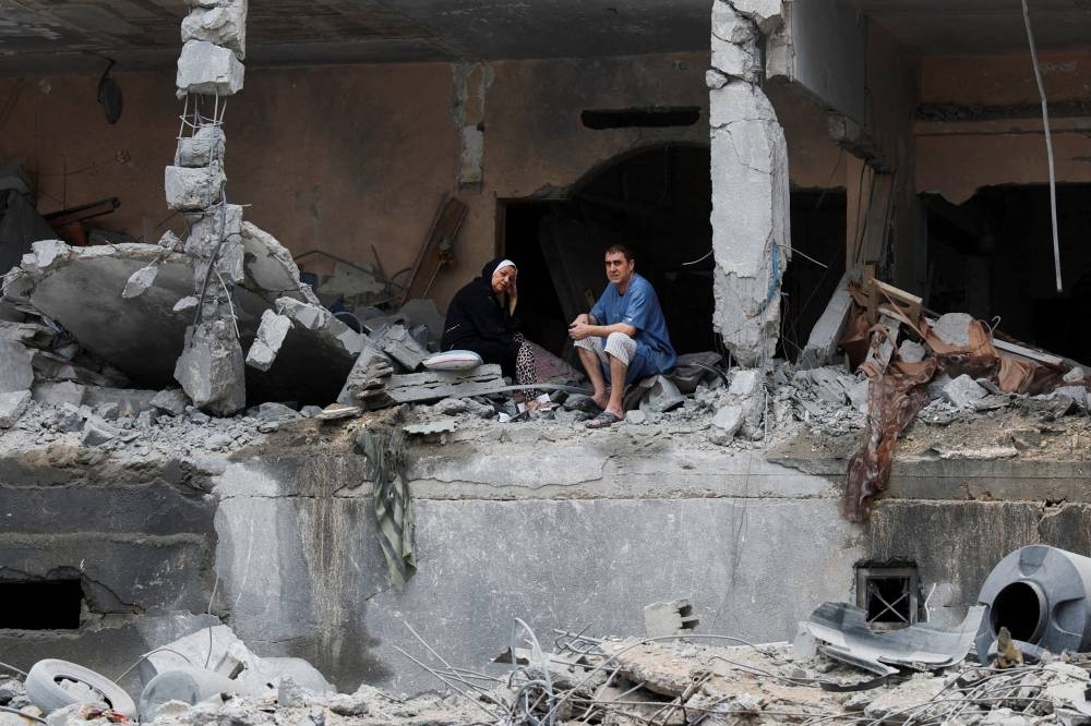 Palestinians sit among the rubble of a damaged residential building, in the aftermath of Israeli strikes, in Gaza City, October 10, 2023.