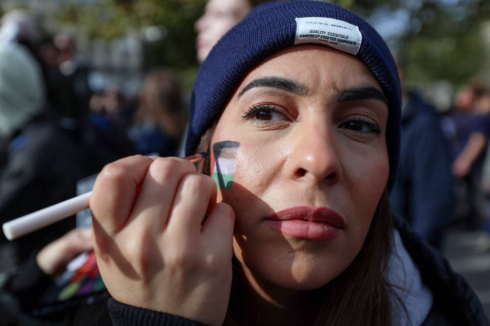 A protestor paints her face with the colours of the Palestinian flag during a demonstration calling for peace in Gaza at Place de la Republique in Paris, Sunday. AFP