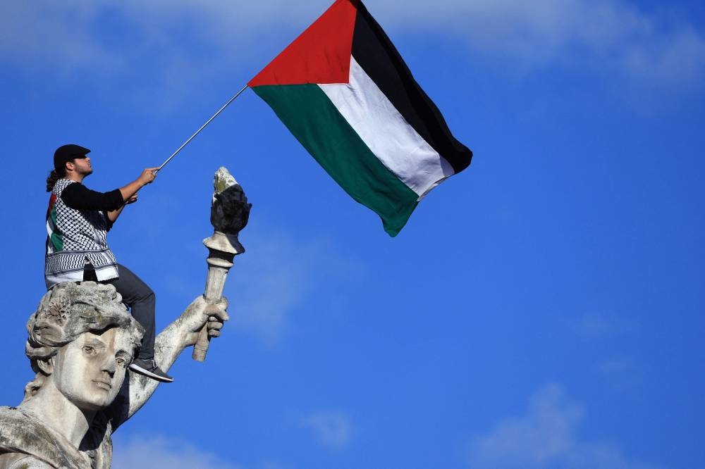 A protestor waves a Palestinian flag sitting on the statue "Le Triomphe de la Republique" (The Triumph of the Republic) during a demonstration calling for peace in Gaza, at Place de la Republique in Paris, Sunday. AFP