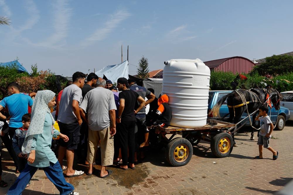 People gather to collect water, as Palestinians, who fled their houses amid Israeli strikes, take shelter in a tent camp at a United Nations-run centre, after Israel's call for more than 1 million civilians in northern Gaza to move south, in Khan Younis in the southern Gaza Strip, on Monday. REUTERS