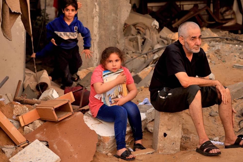 A Palestinian girl clutches salvaged books as people look for survivors in the rubble of a destroyed building hit in an Israeli strike in Khan Yunis in the southern Gaza Strip on Tuesday. AFP