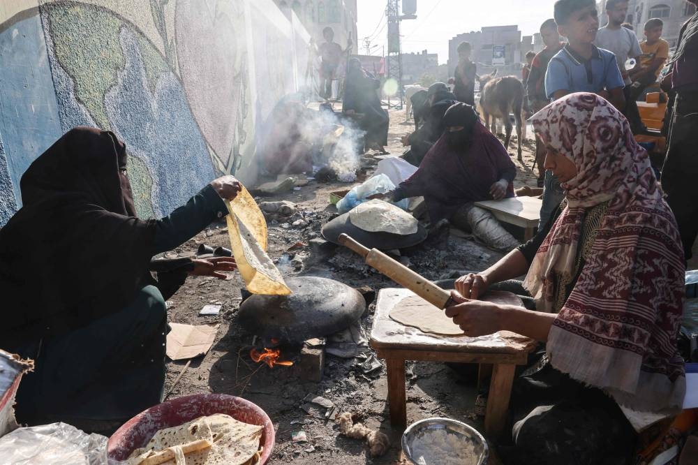 Palestinian women make traditional unleavened bread on an open fire at a shelter for displaced families mainly from the north of the Gaza Strip, at a UN-run school in Rafah, in the southern Gaza Strip on Friday. AFP