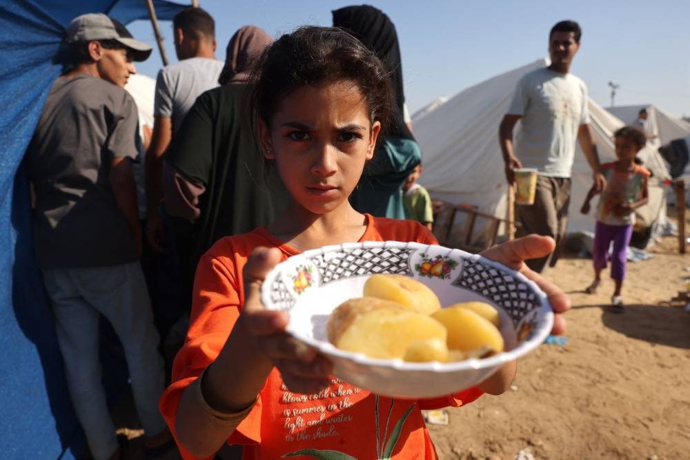 A displaced Palestinian girl, who fled her home amid Israeli strikes, shows her plate of food collected at a food distribution point as she and her family shelter in tents set up in a United Nations-run center in Khan Yunis, in the southern Gaza Strip on October 26. AFP