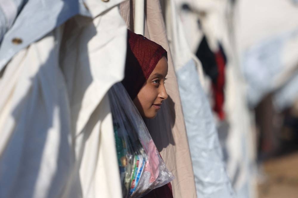 A displaced Palestinian girl, who fled her home amid Israeli strikes, peeks out of her tent shelter set up in a United Nations-run center, following Israel's call for more than 1 million residents in northern Gaza to move south, in Khan Yunis, in the southern Gaza Strip on October 26. AFP