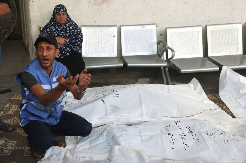 A Palestinian employee working for the United Nations as a guard, reacts as squates next to the covered bodies of his relatives from the al-Hamayda family after they were brought to the Al-Najjar Hospital following an Israeli air strike on Rafah in southern Gaza Strip on Friday. AFP