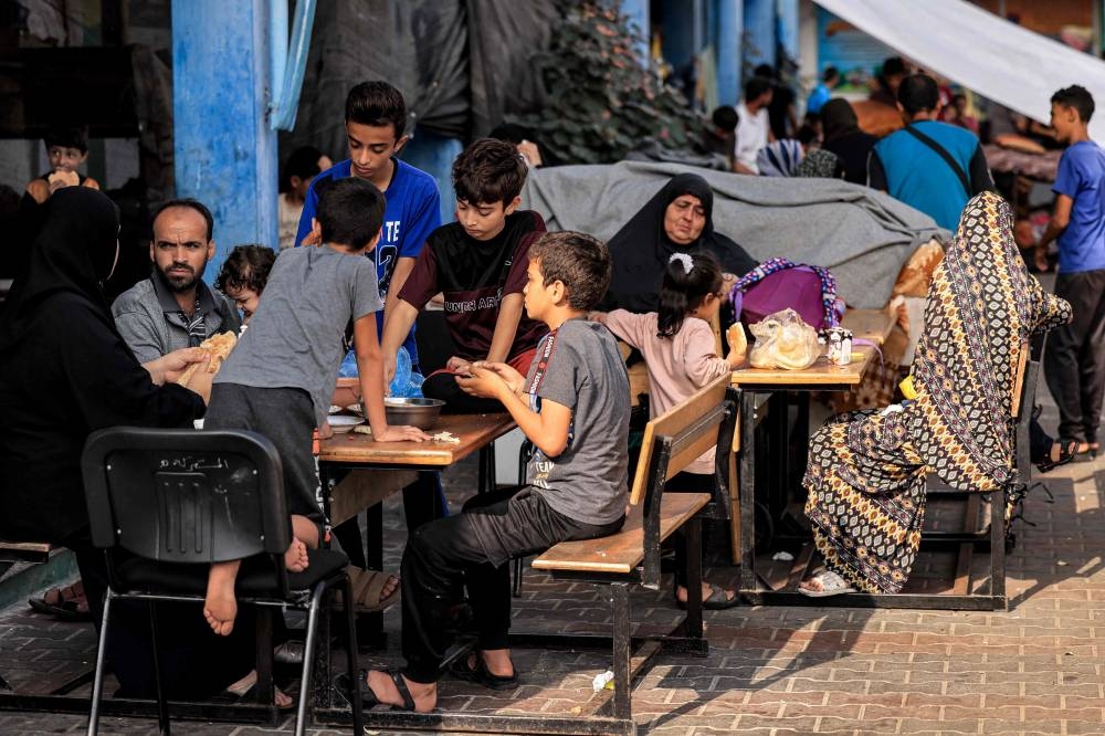 Members of a family sit together in the playground of a school run by the United Nations Relief and Works Agency for Palestine Refugees (UNRWA) agency that has been converted into a shelter for displaced Palestinians in Khan Yunis in the southern Gaza Strip on October 25. AFP