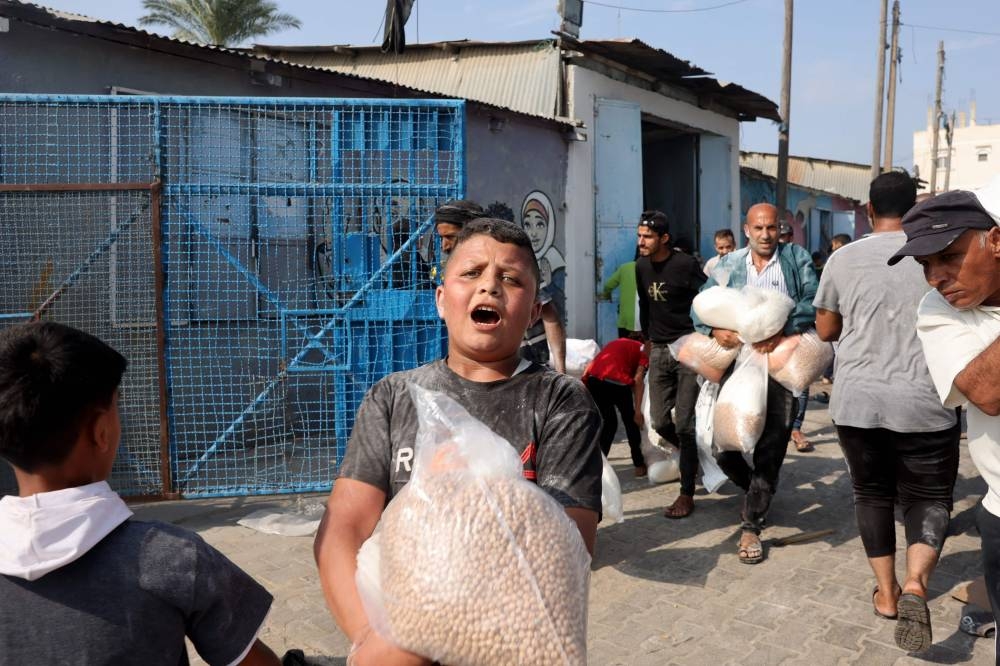 A Palestinian boy holds a bag of chickpeas collected from a UN-run aid supply center, distributing food to local Palestinians and people displaced following Israel's call for more than 1 million residents in northern Gaza to move south for their safety, in Deir al-Balah on Saturday. AFP