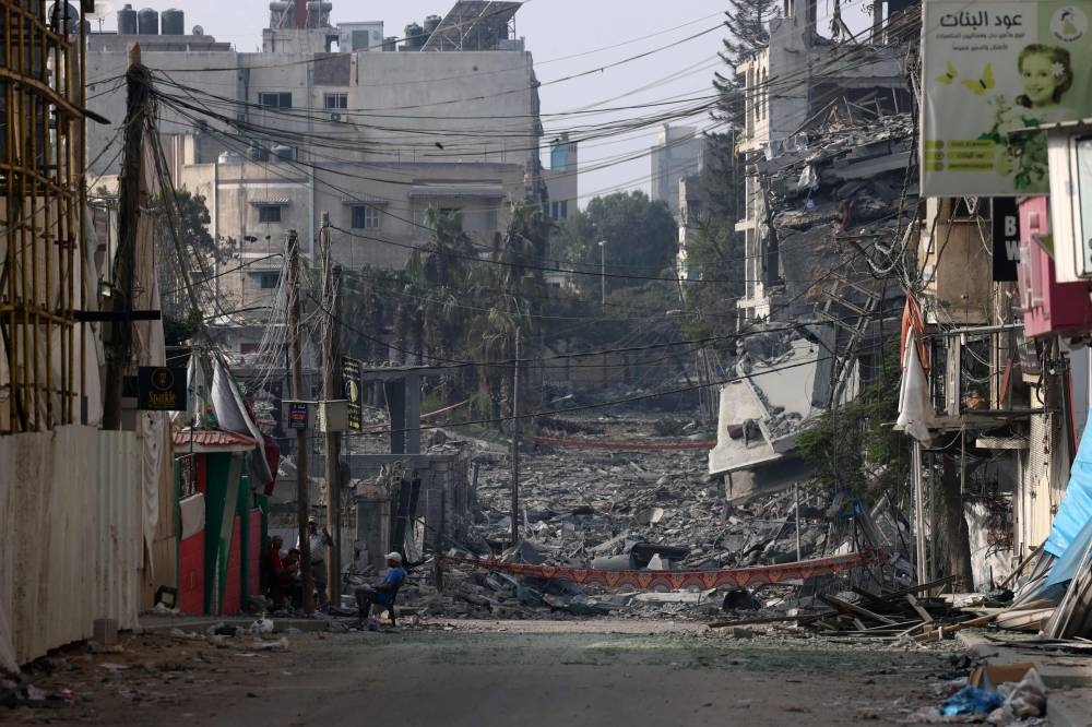 A man sits in front of buildings destroyed by Israeli strikes in Gaza City on Saturday. AFP