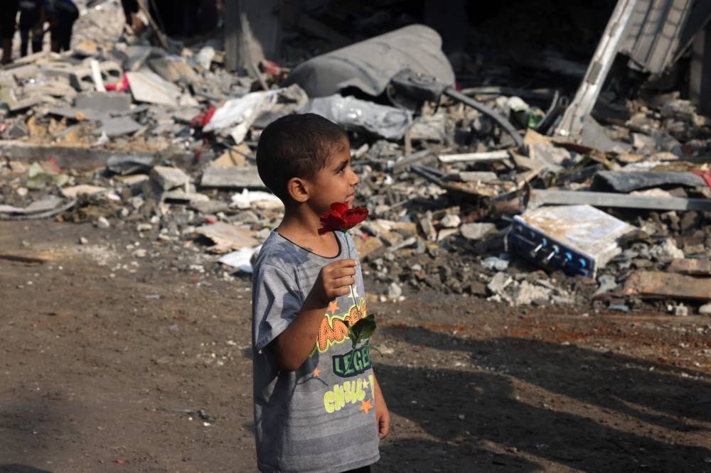 A young boy holds a fake flower found amid the rubble of a building in the aftermath of Israeli strikes in Gaza City on Saturday. AFP