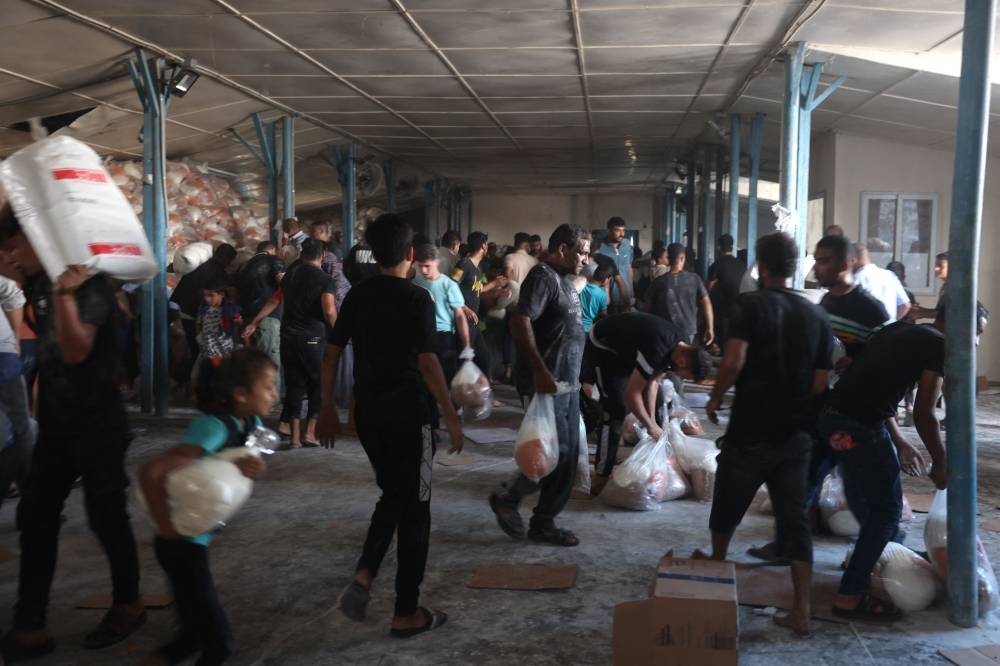 Palestinians collect bags of dried pulses from a UN-run aid supply center, distributing food to local Palestinians and people displaced following Israel's call for more than 1 million residents in northern Gaza to move south for their safety, in Deir al-Balah on Saturday. AFP