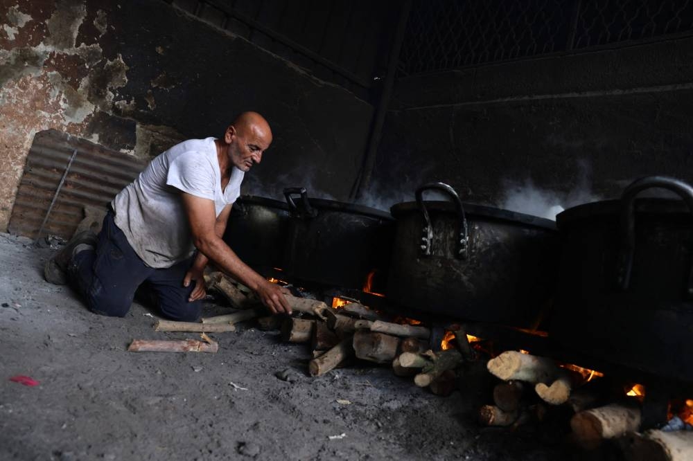 A Palestinian man adds fire wood under large pots simmering of food which will be distributed to displaced families following Israel's call for more than 1 million residents in northern Gaza to move south, in Rafah, in the southern Gaza Strip Saturday. AFP