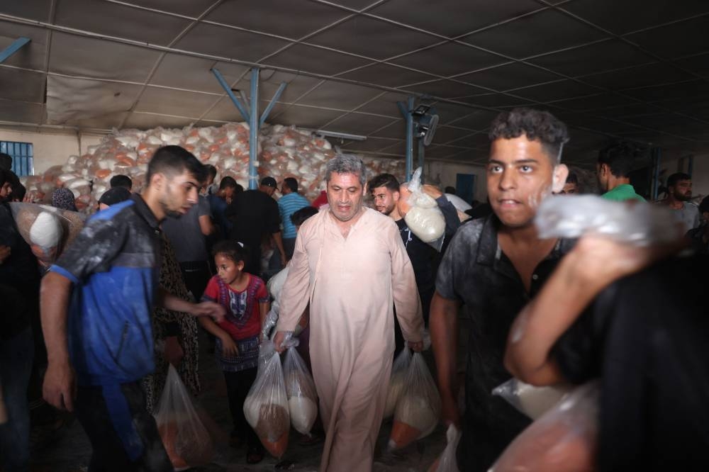 Palestinians collect bags of dried pulses from a UN-run aid supply center, distributing food to local Palestinians and people displaced following Israel's call for more than 1 million residents in northern Gaza to move south for their safety, in Deir al-Balah on Saturday. AFP