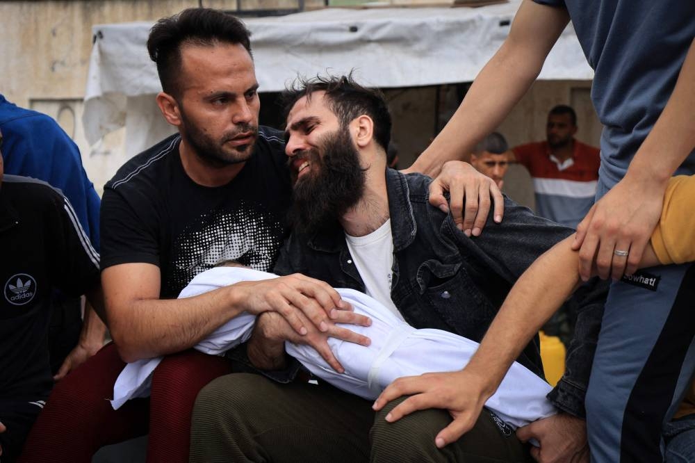 The father of a young boy from the al-Aqad family, reacts as he holds the body of his child, killed in an Israeli strike on Khan Yunis in the southern Gaza Strip, before his burial on Monday. AFP
