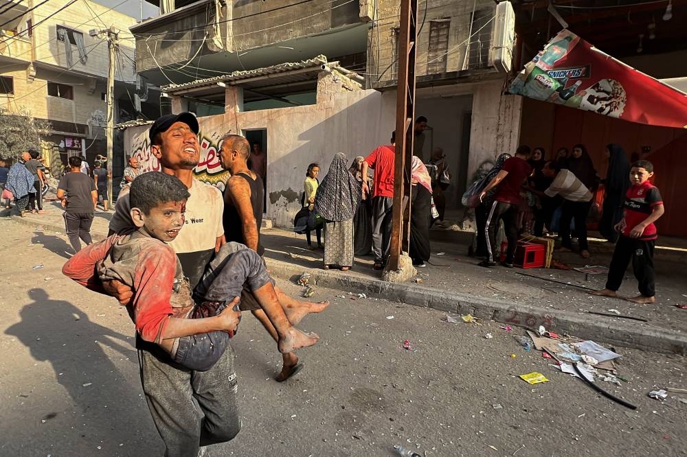 A Palestinian carries a child casualty at the site of Israeli strikes on houses, in Gaza City Saturday. REUTERS