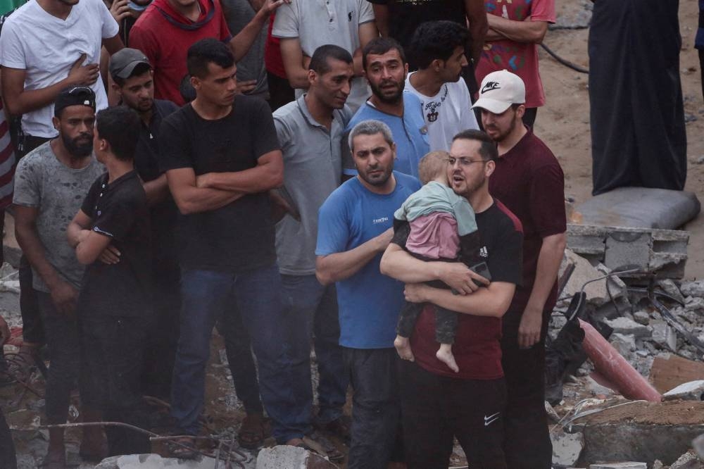 A Palestinian man holds a dead child recovered from the rubble as others conduct search and rescue operations at the site of Israeli strikes on a residential building, in the central Gaza Strip, on Tuesday. REUTERS