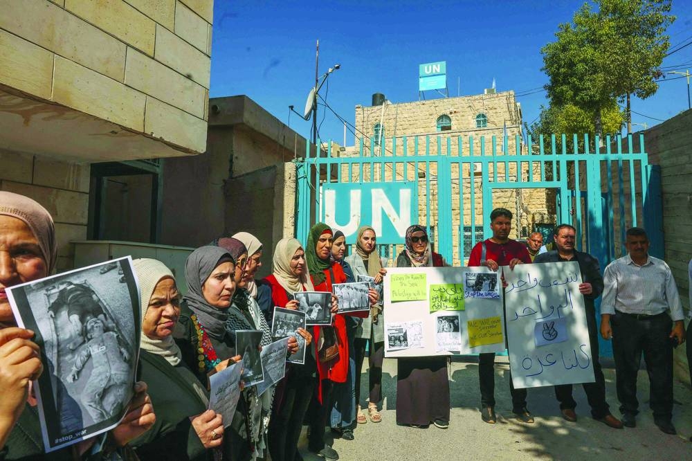 Palestinians lift placards during a rally in front of the UN Relief and Works Agency for Palestine Refugees (UNRWA) offices in Hebron in the occupied West Bank, on Tuesday, in support of Gaza.