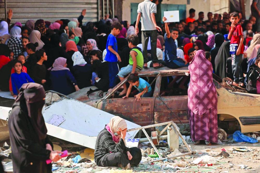 Children play in a charred car as people queue for bread in front of a bakery that was partially destroyed in an Israeli strike, at the Nuseirat refugee camp in the central Gaza Strip.