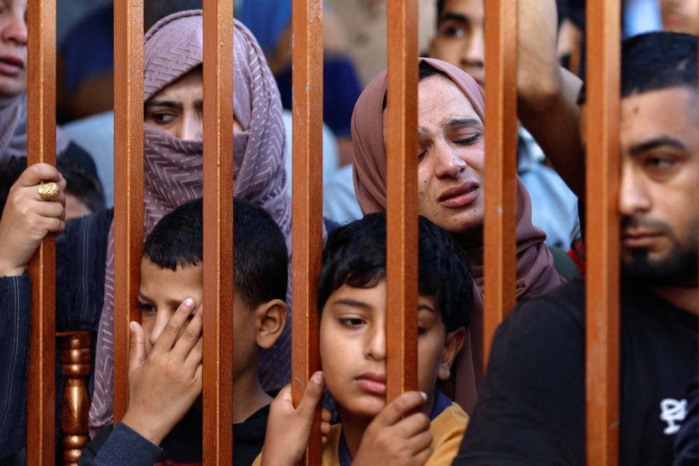 People react from behind a gate as the bodies of Palestinians killed by Israeli strikes are laid on the ground at a hospital, in Khan Younis in the southern Gaza Strip, on Friday. REUTERS