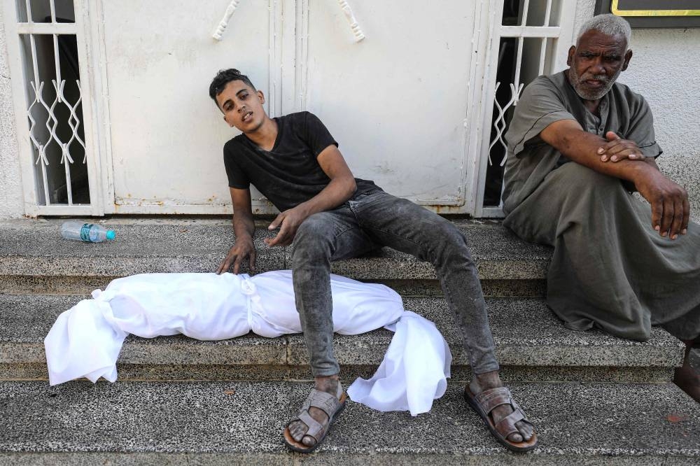 A Palestinian man sits on a step with the body of a child wrapped in a shroud next to him, outside a hospital following Israel's bombardment of Gaza City's eastern suburb of Shujaiya on Saturday. AFP
